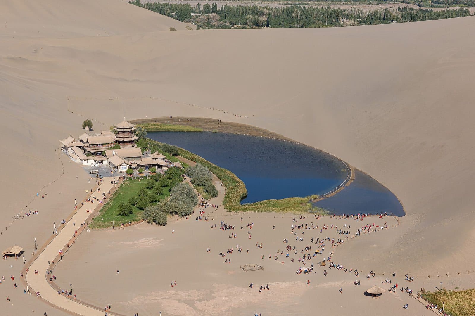 Crescent Lake, a curved blue pool with pavilions on its shore, seen from the top of the sand dunes