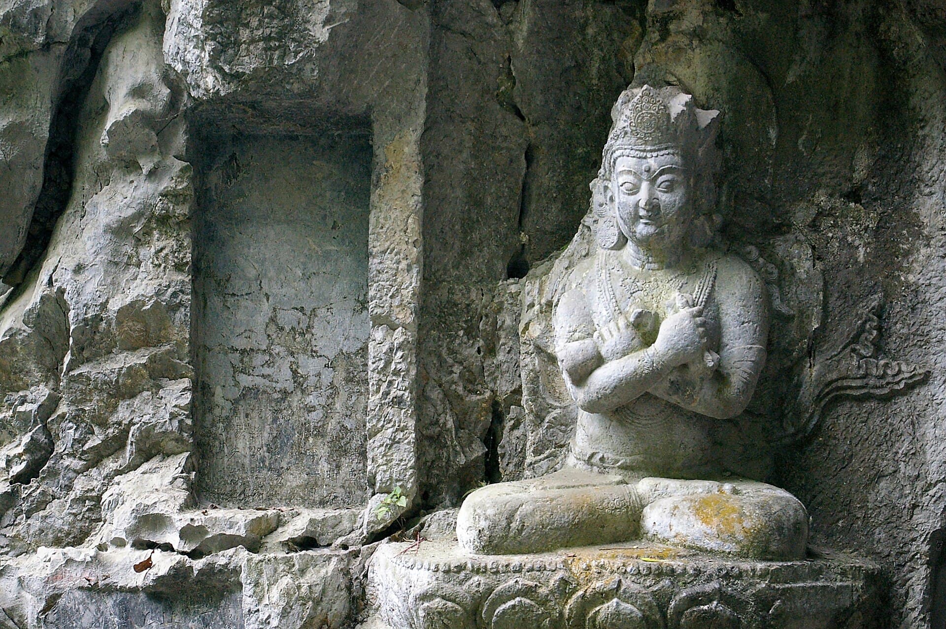 A seated Buddha carved into the grey limestone of Feilai Feng, with smaller figures in niches beside it