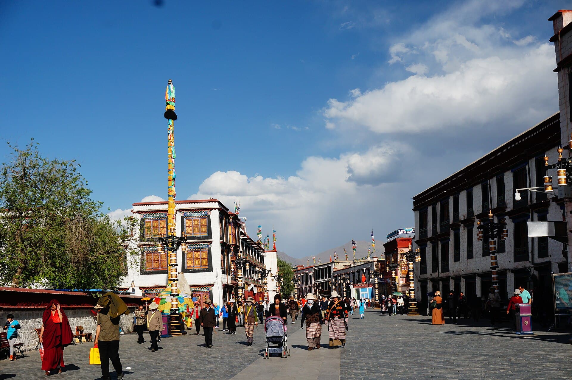 A street of whitewashed Tibetan buildings with colourful window frames in Lhasa's old town, with people walking and a prayer pole