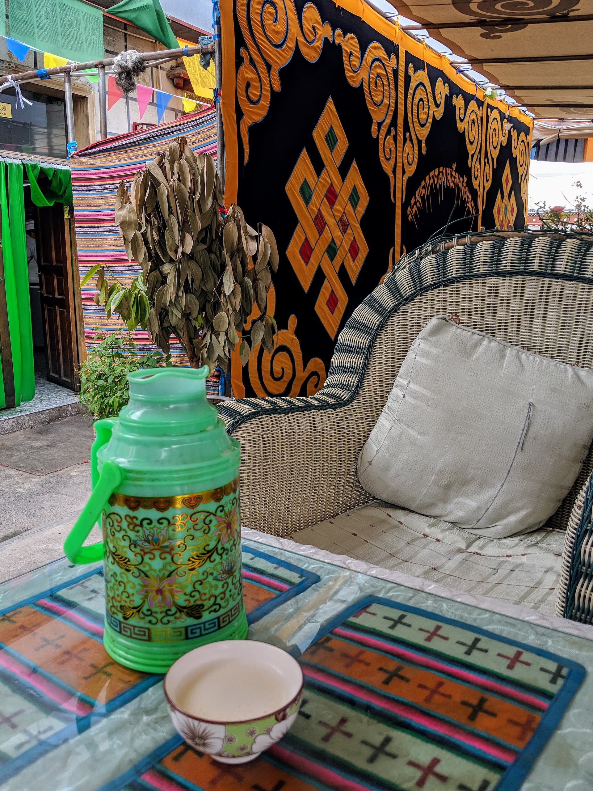 A green thermos flask and a small bowl of pale butter tea on a low table in a Lhasa teahouse