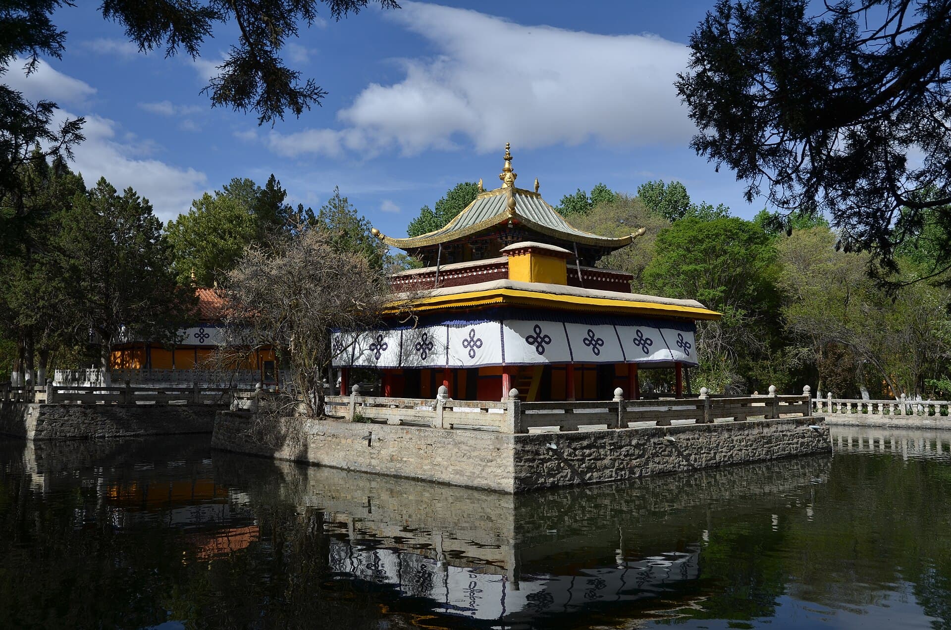 A yellow-roofed pavilion of Norbulingka, the summer palace, standing in a pond surrounded by trees