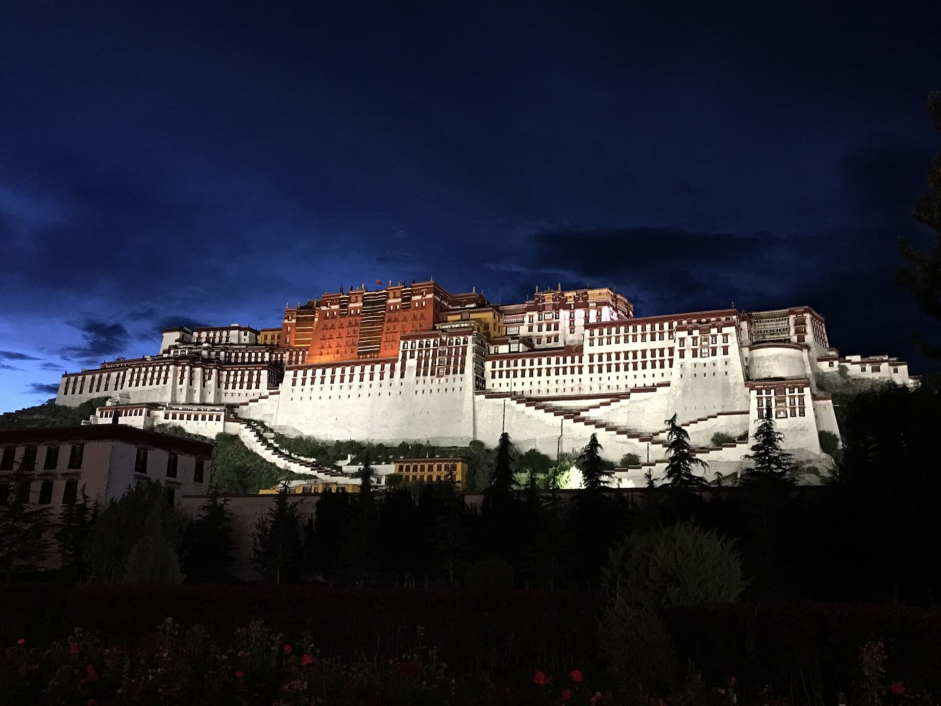 The Potala Palace lit up at dusk on Red Hill, its white and red walls glowing against a deep blue sky