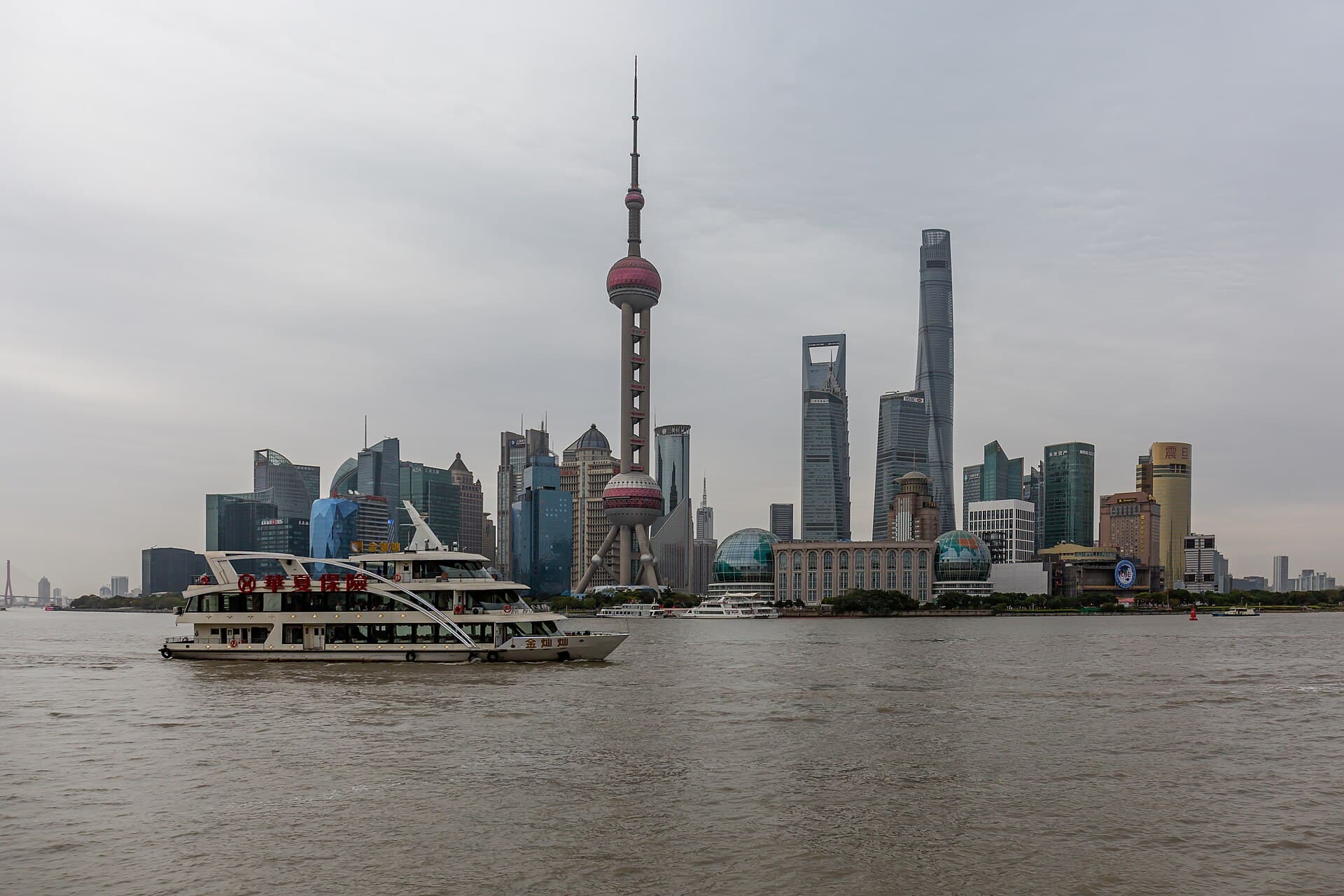 A commuter ferry crossing the grey Huangpu River with the Lujiazui towers behind it