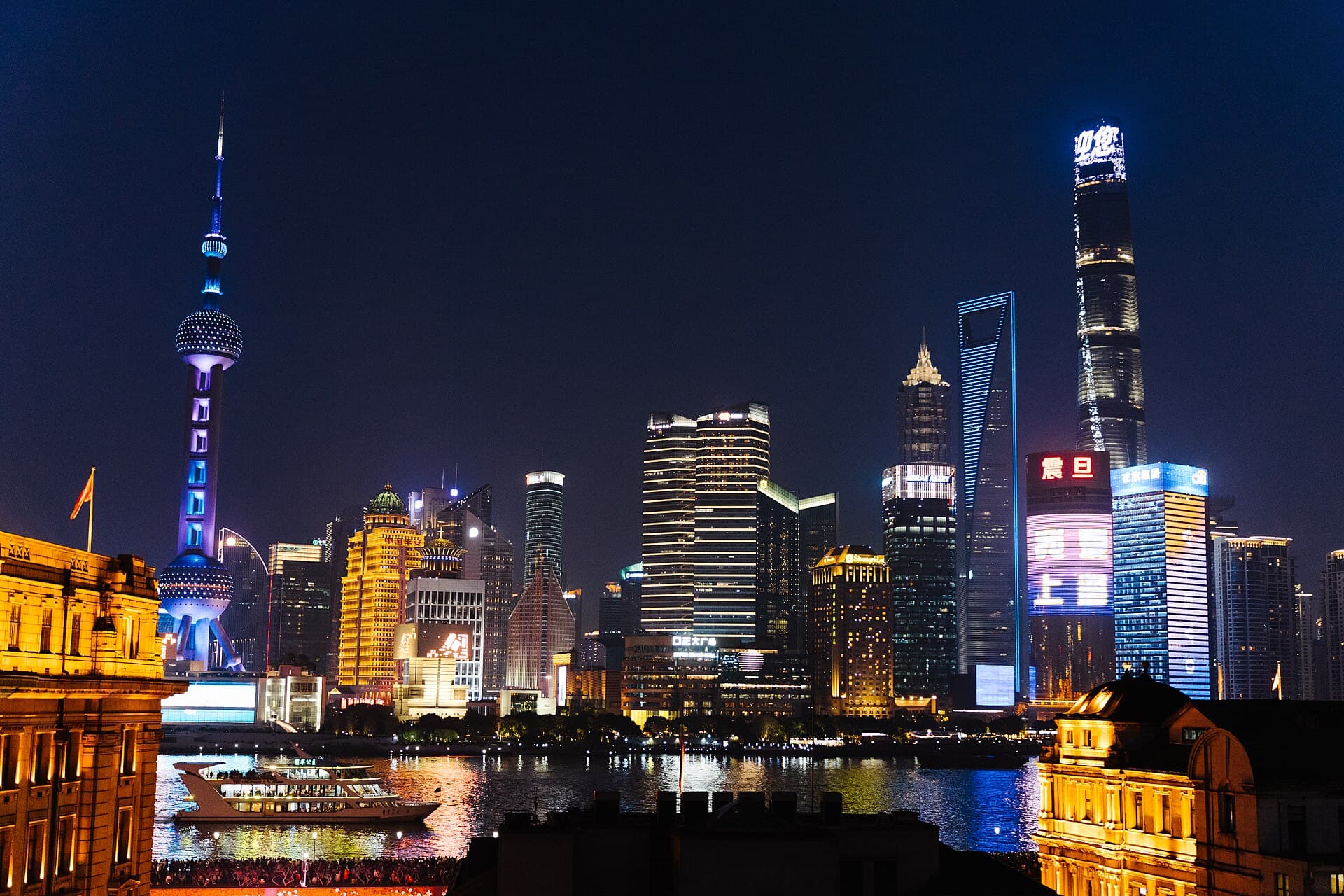 The lit-up Pudong skyline at night across the Huangpu River, with the Oriental Pearl Tower on the left and the Shanghai Tower on the right