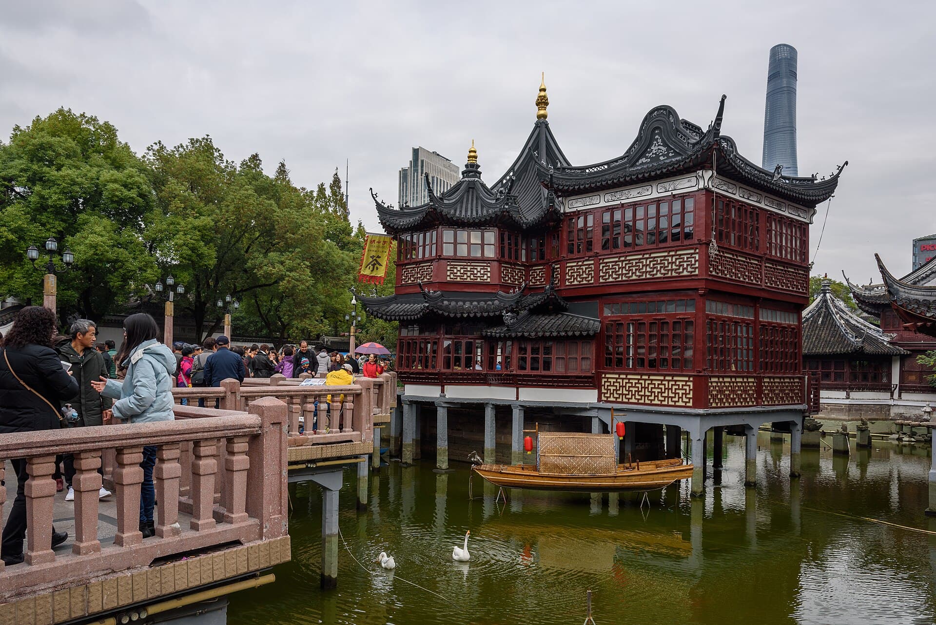 The Huxinting teahouse standing in a pond on zigzag bridges, with the Shanghai Tower rising behind the old roofs