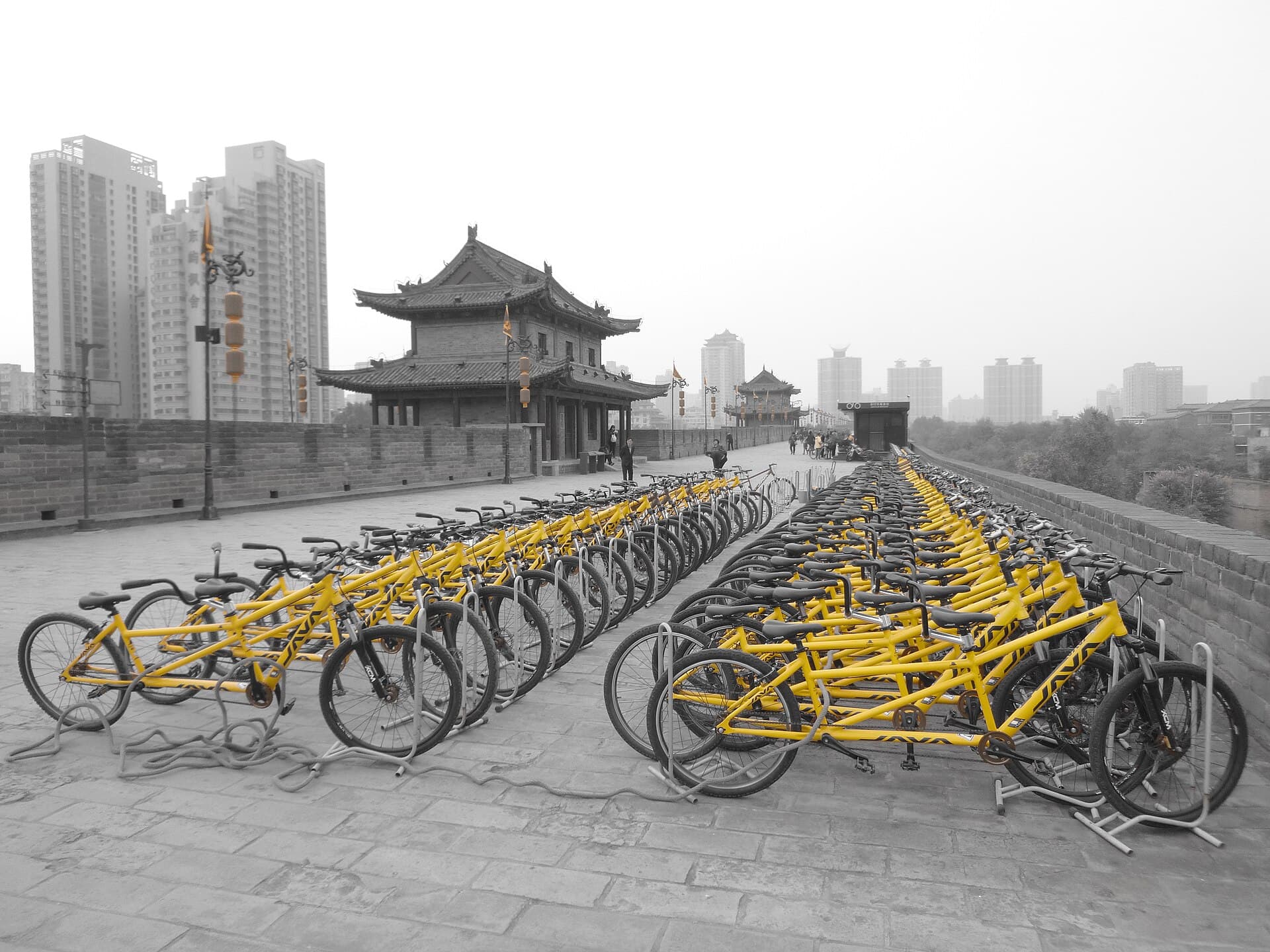 Rows of yellow rental bicycles lined up on the wide brick top of Xi'an's city wall, with a gate tower behind