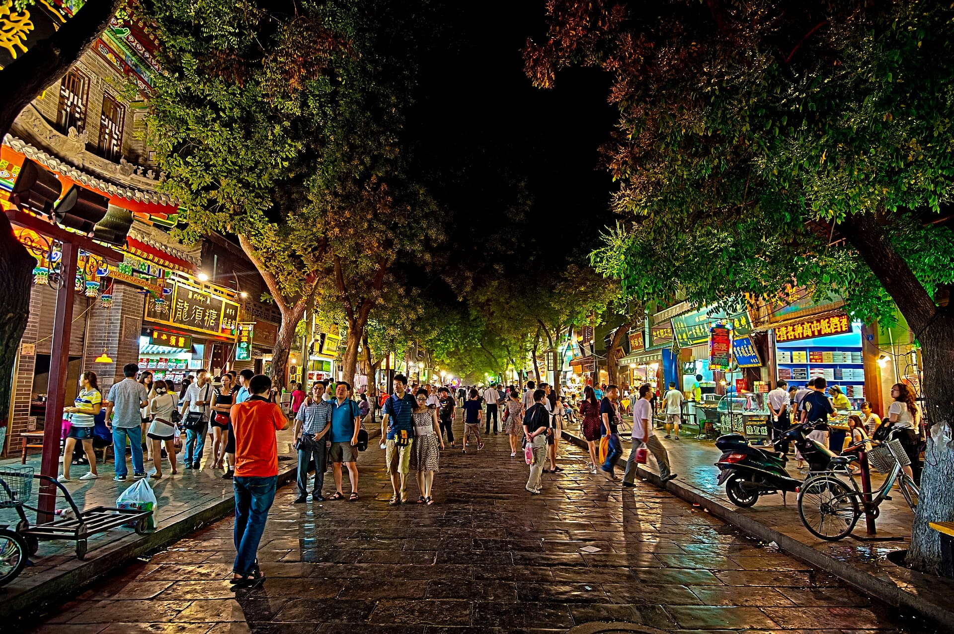 The tree-lined main street of Xi'an's Muslim Quarter at night, crowded and lit by food-stall signs