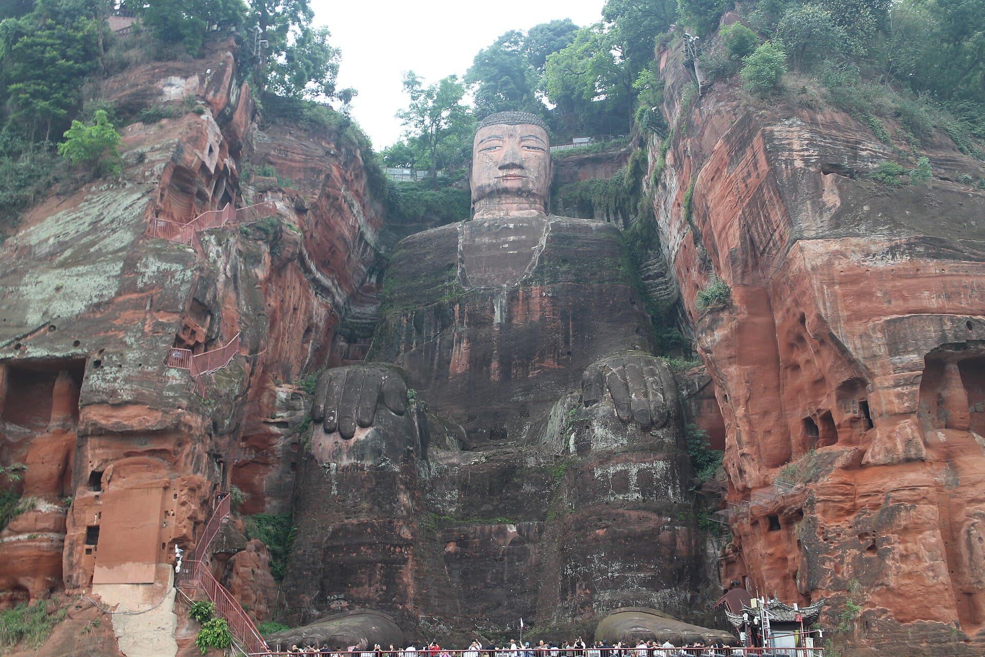 The 71-metre seated Leshan Giant Buddha carved into a red sandstone cliff, with visitors on the stairs beside it