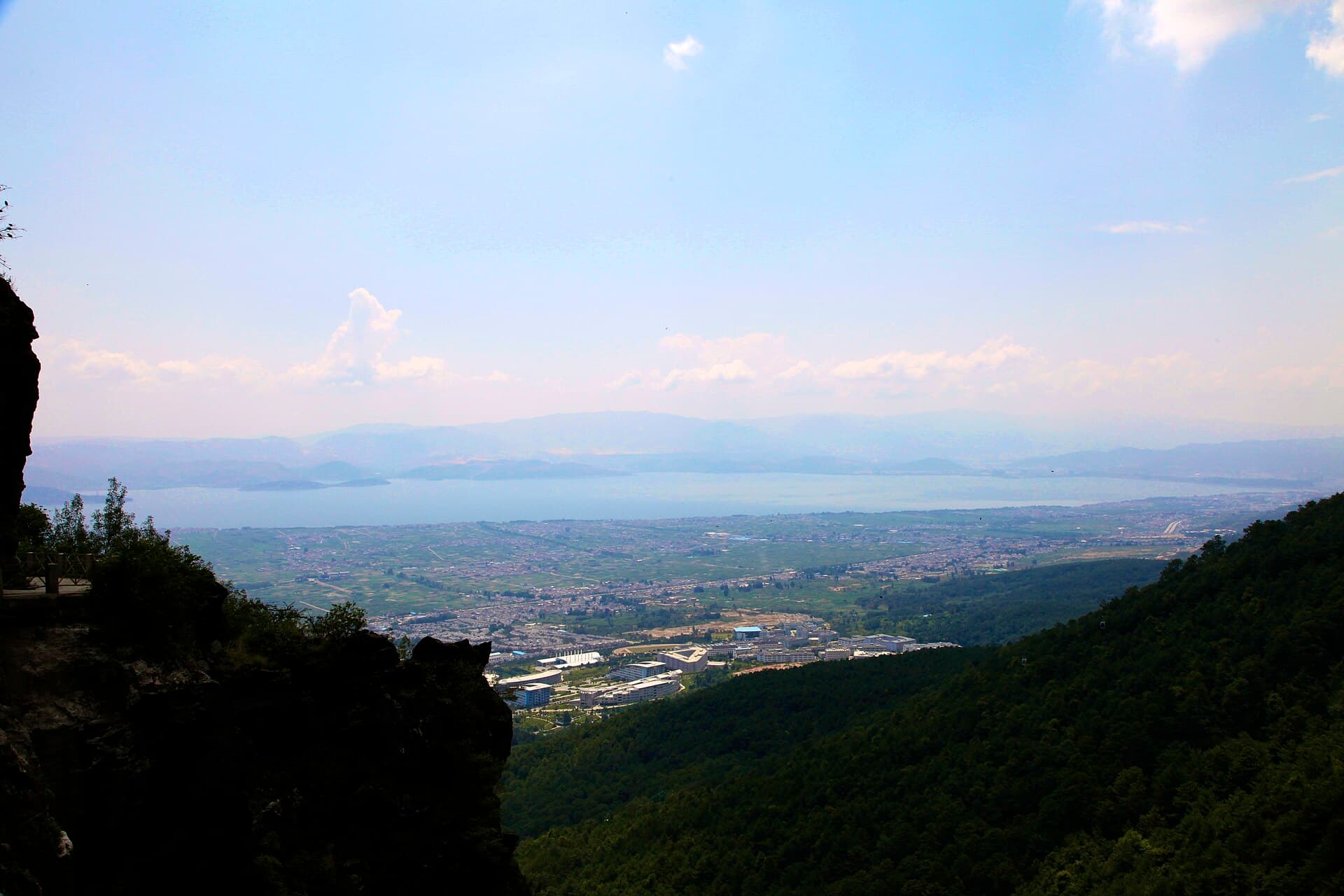 The view down from a shaded trail on Cangshan across fields to Erhai Lake under a cloudy sky