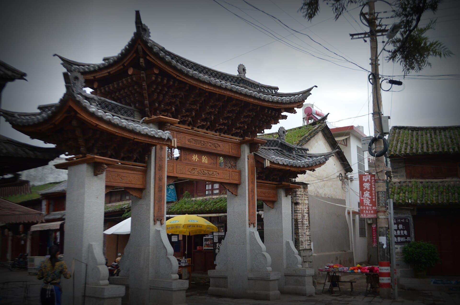 A carved and painted Bai stone gateway leading into the square of Xizhou, with grey-tiled houses either side