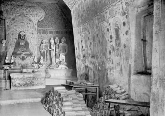 Black-and-white photograph of bundles of manuscripts piled up inside Cave 16 at the Mogao Caves in 1907