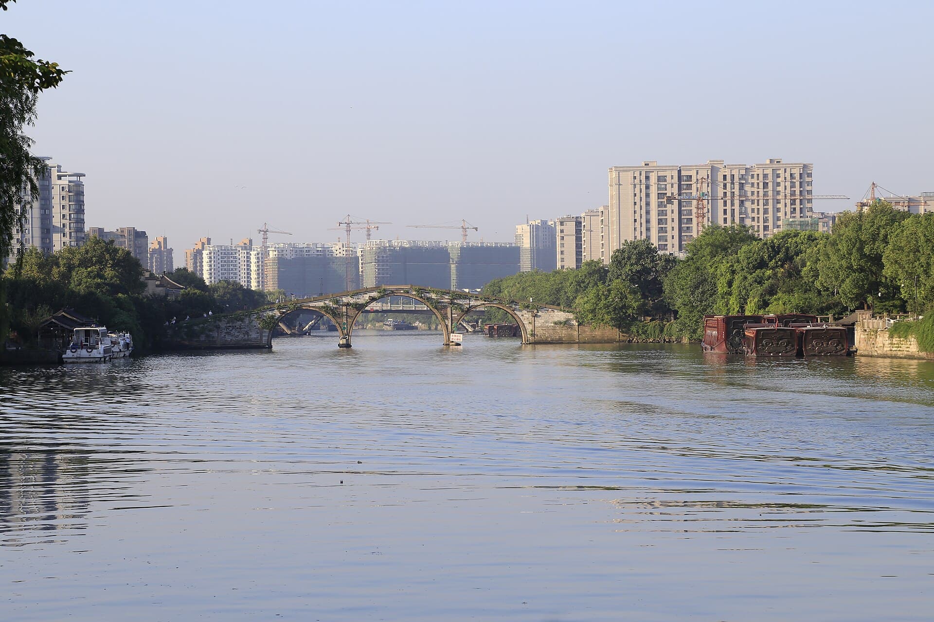 The three stone arches of Gongchen Bridge over the Grand Canal in Hangzhou, with modern towers behind