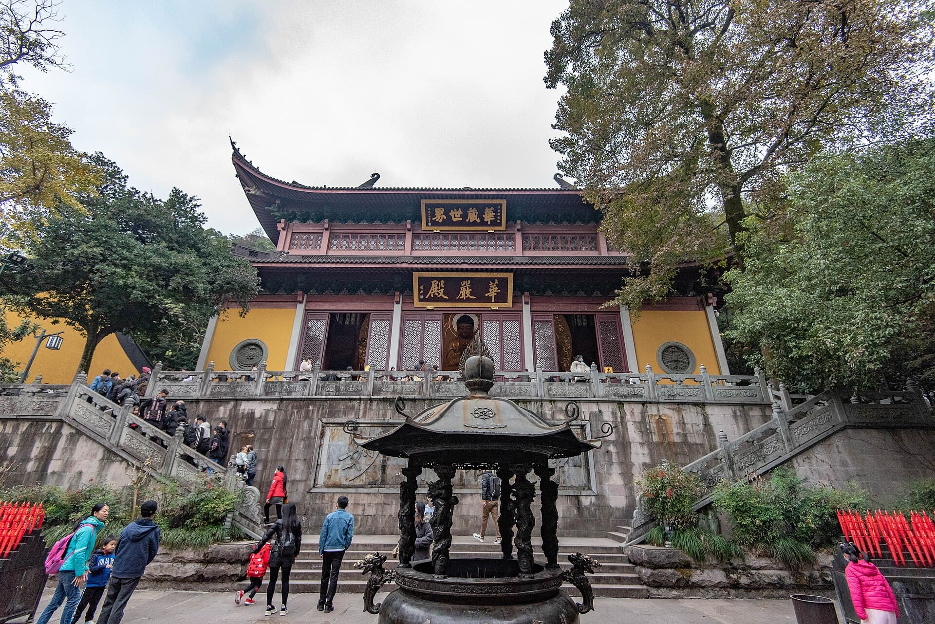 The yellow-walled Huayan Hall of Lingyin Temple above stone steps, with visitors and an incense burner in front